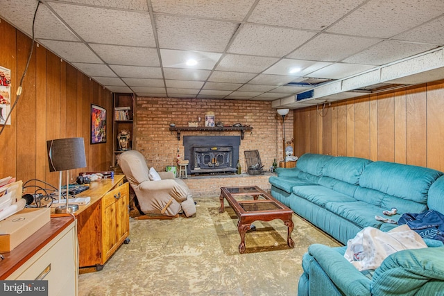 carpeted living room with a drop ceiling, wood walls, and brick wall