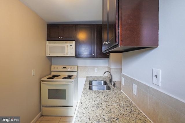 kitchen with sink, light tile patterned floors, light stone countertops, white appliances, and dark brown cabinetry