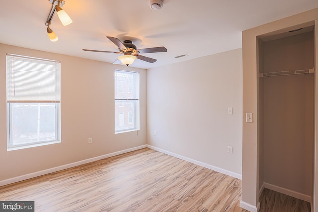 unfurnished bedroom with a closet, ceiling fan, track lighting, and light wood-type flooring