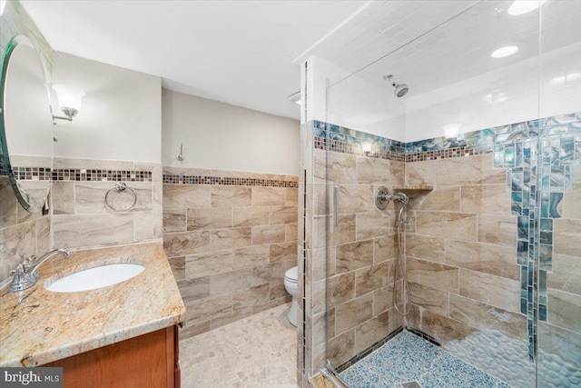 bathroom featuring vanity, toilet, tiled shower, and tile walls