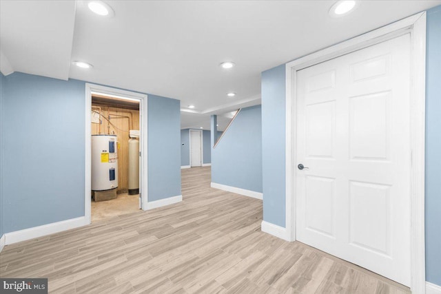 basement with light hardwood / wood-style floors and water heater