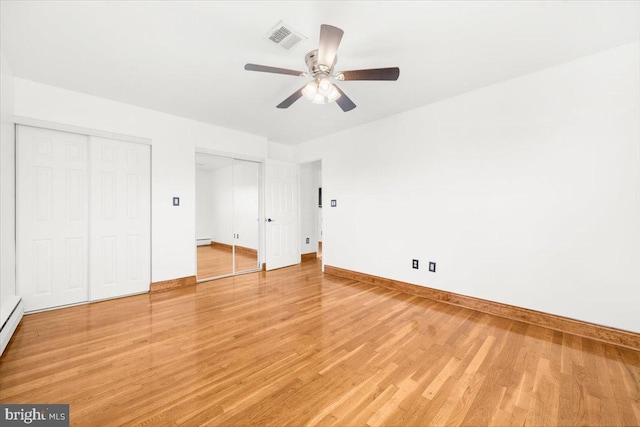 unfurnished bedroom featuring hardwood / wood-style floors, ceiling fan, baseboard heating, and two closets