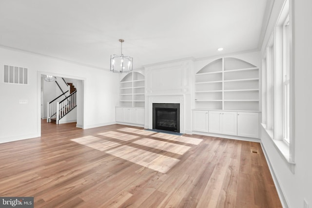 unfurnished living room featuring built in shelves, light hardwood / wood-style floors, and a chandelier