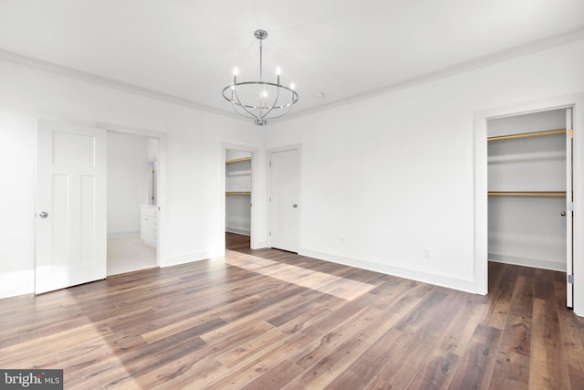 unfurnished bedroom with dark wood-type flooring, an inviting chandelier, crown molding, a spacious closet, and connected bathroom