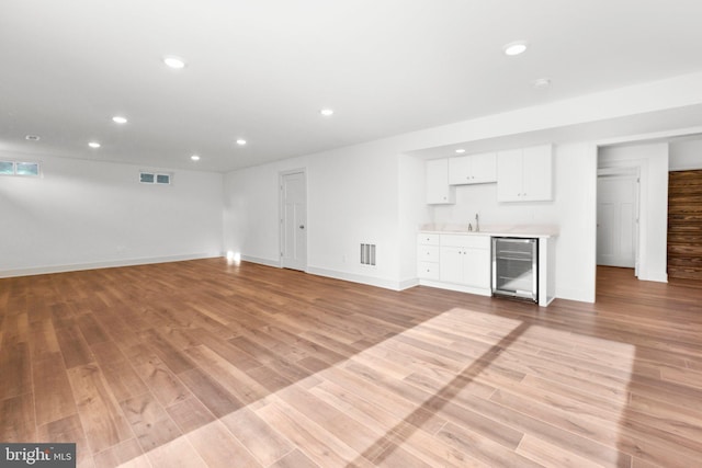 unfurnished living room with light wood-type flooring, wine cooler, and sink