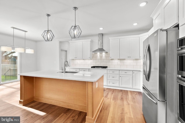 kitchen with wall chimney exhaust hood, an island with sink, light hardwood / wood-style floors, white cabinetry, and stainless steel appliances