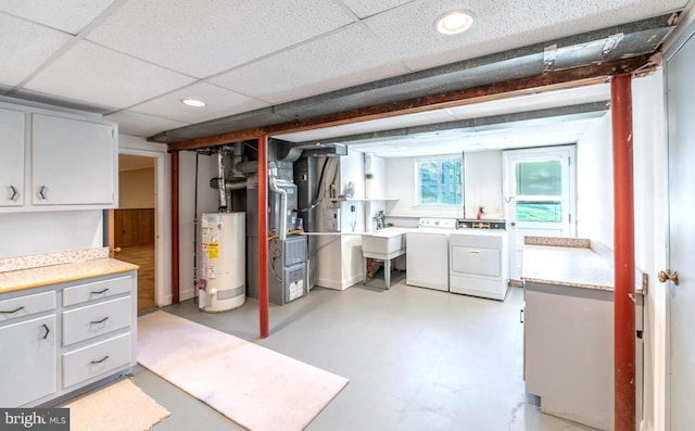 basement with a drop ceiling, gas water heater, sink, washing machine and dryer, and heating unit