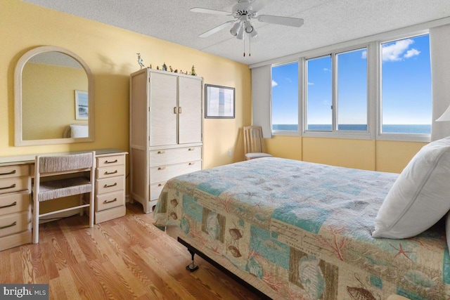 bedroom featuring ceiling fan, a water view, light wood-type flooring, and a textured ceiling