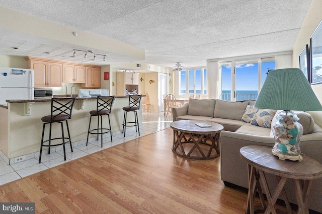 living room with a textured ceiling, ceiling fan, sink, light tile patterned floors, and a water view