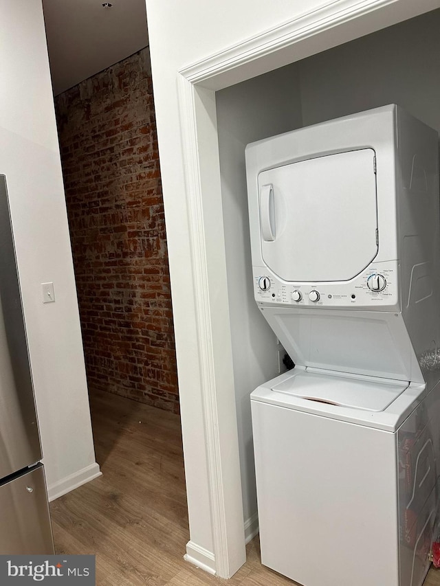 clothes washing area with stacked washer / dryer, brick wall, and light hardwood / wood-style flooring