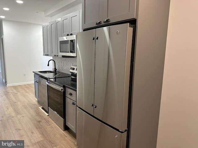 kitchen with decorative backsplash, appliances with stainless steel finishes, gray cabinetry, sink, and light hardwood / wood-style flooring