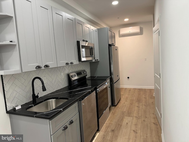 kitchen with decorative backsplash, appliances with stainless steel finishes, a wall mounted AC, sink, and light hardwood / wood-style floors