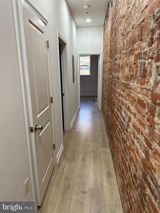 corridor featuring light wood-type flooring and brick wall