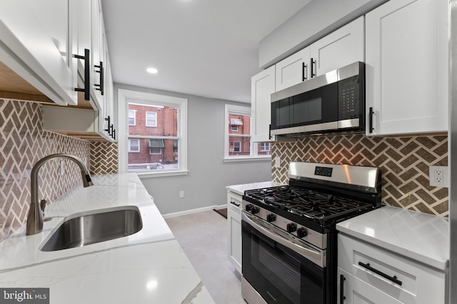 kitchen with appliances with stainless steel finishes, white cabinetry, light stone counters, and sink