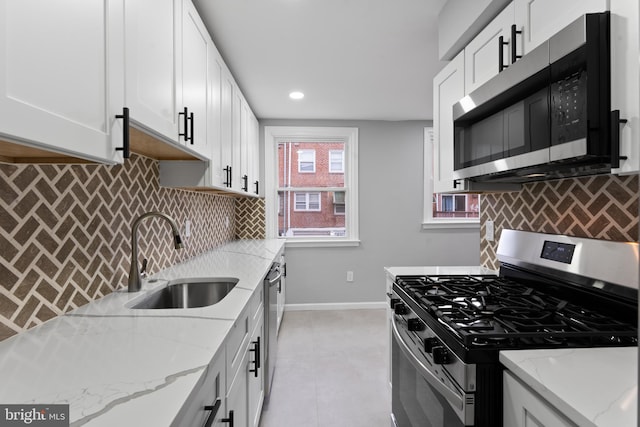 kitchen featuring light stone countertops, decorative backsplash, stainless steel appliances, sink, and white cabinetry