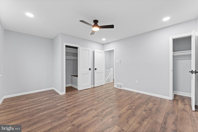 unfurnished bedroom featuring dark hardwood / wood-style flooring, ceiling fan, and multiple closets