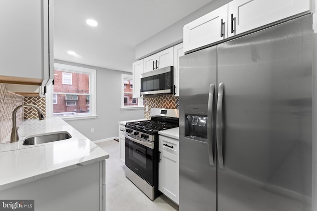 kitchen featuring decorative backsplash, light stone countertops, stainless steel appliances, sink, and white cabinets