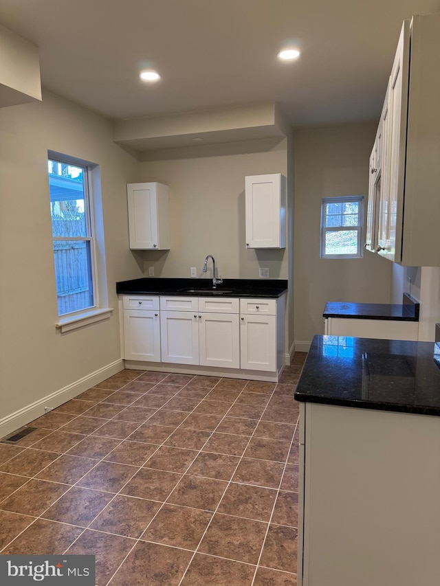 kitchen with white cabinets, dark tile patterned flooring, a healthy amount of sunlight, and sink