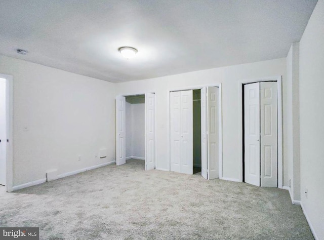 unfurnished bedroom with light carpet, a textured ceiling, and multiple closets