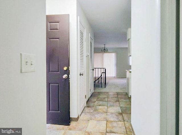 corridor with light carpet and a notable chandelier