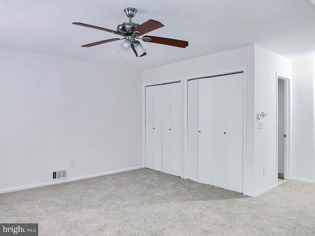 unfurnished bedroom with two closets, light colored carpet, and ceiling fan