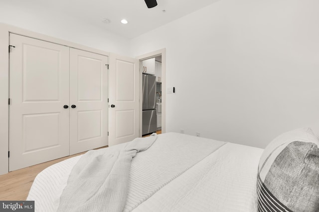 bedroom with light hardwood / wood-style flooring, stainless steel refrigerator, a closet, and ceiling fan