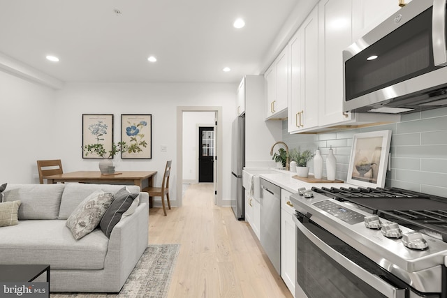 kitchen featuring backsplash, light hardwood / wood-style flooring, white cabinets, and stainless steel appliances