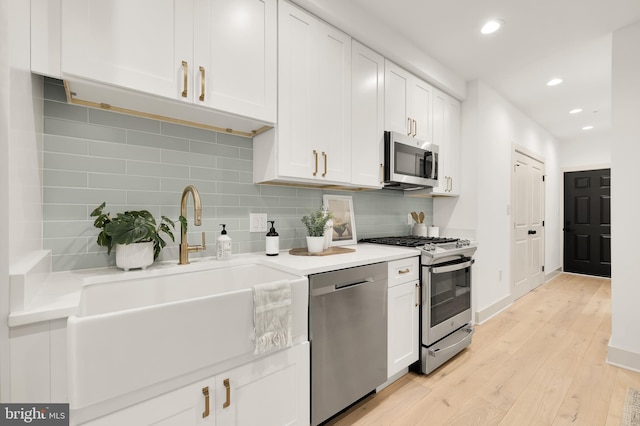 kitchen featuring appliances with stainless steel finishes, light wood-type flooring, tasteful backsplash, sink, and white cabinets