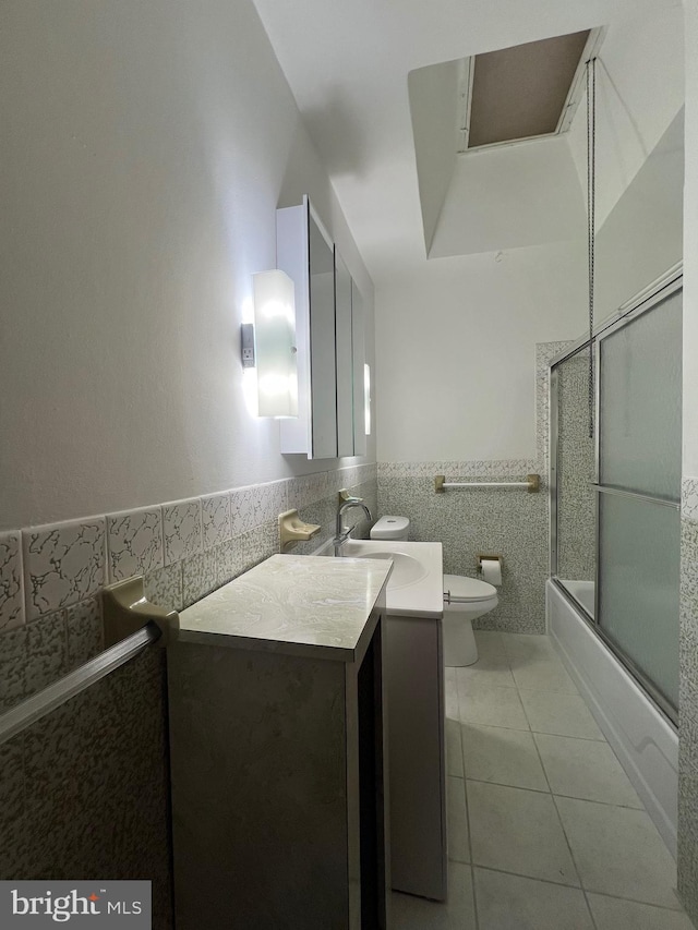 full bathroom with vanity, tile patterned floors, combined bath / shower with glass door, toilet, and tile walls