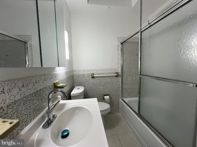 full bathroom with tile patterned floors, bath / shower combo with glass door, toilet, vanity, and tile walls