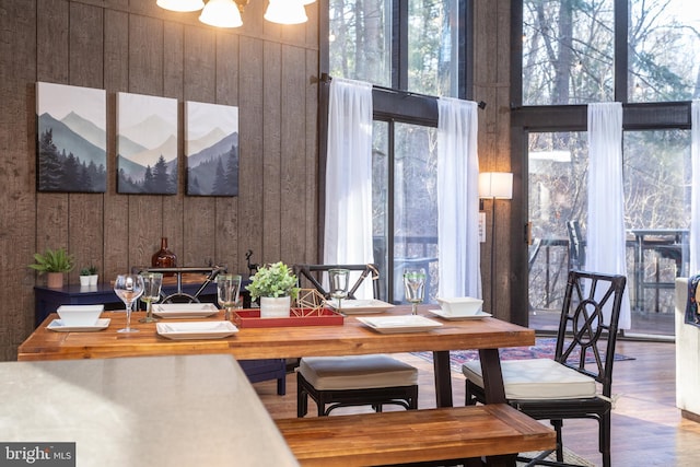 dining area with a notable chandelier, wood-type flooring, and wooden walls