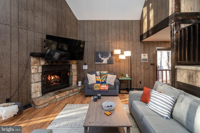 living room featuring a fireplace, high vaulted ceiling, light hardwood / wood-style flooring, and wood walls