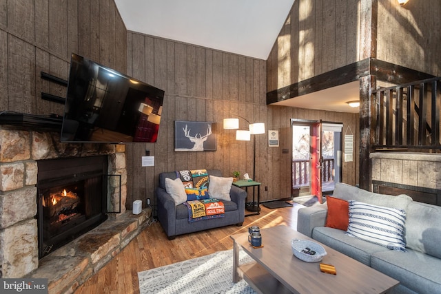 living room with light wood-type flooring, wooden walls, high vaulted ceiling, and a stone fireplace