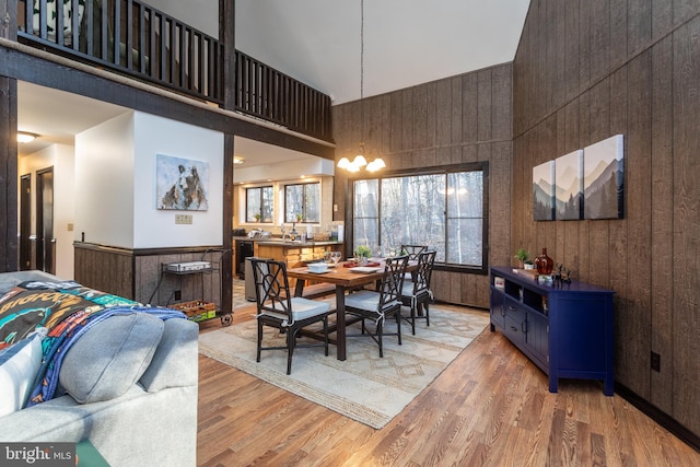 dining space with wooden walls, a towering ceiling, and light wood-type flooring