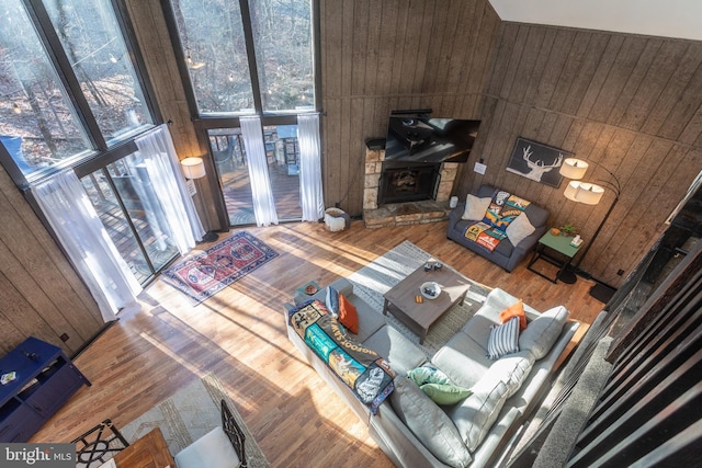 living room with wood walls, wood-type flooring, a towering ceiling, and a fireplace