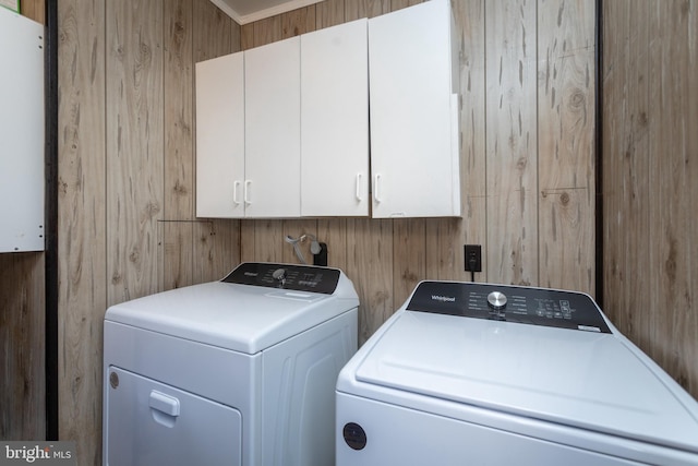 laundry area featuring cabinets, wooden walls, and washing machine and clothes dryer