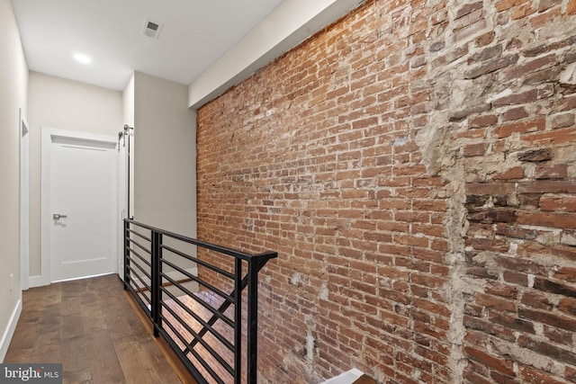 hallway with dark hardwood / wood-style flooring, a barn door, and brick wall