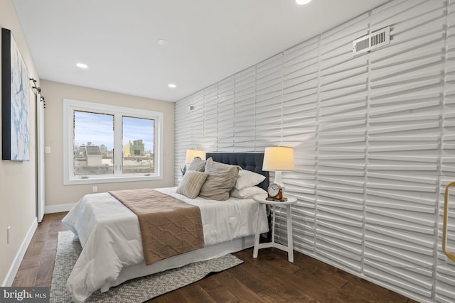 bedroom with a barn door and dark wood-type flooring