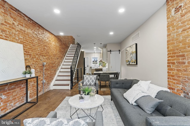 living room with brick wall, a barn door, and hardwood / wood-style flooring