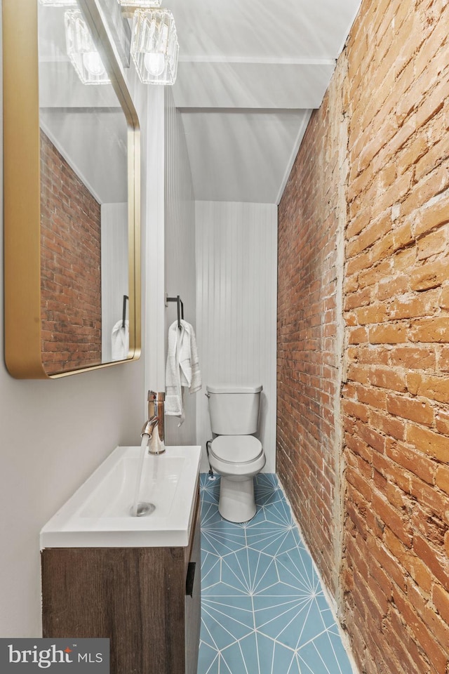 bathroom featuring brick wall, vanity, and toilet