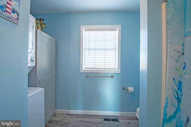 laundry room featuring stacked washing maching and dryer and light hardwood / wood-style flooring