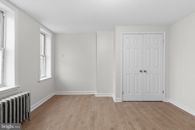 unfurnished bedroom with multiple windows, a closet, radiator heating unit, and light hardwood / wood-style flooring