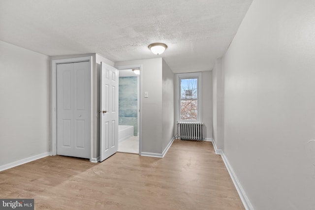 interior space featuring ensuite bath, radiator heating unit, light hardwood / wood-style flooring, a textured ceiling, and a closet