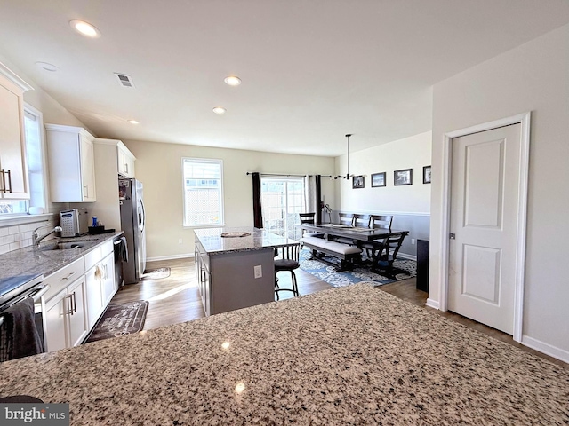 kitchen featuring a breakfast bar, a center island, backsplash, hanging light fixtures, and white cabinetry