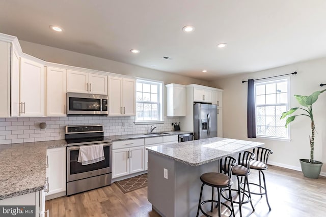 kitchen featuring appliances with stainless steel finishes, a kitchen island, sink, light hardwood / wood-style flooring, and white cabinetry