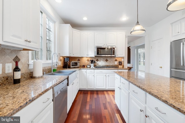 kitchen with light stone countertops, white cabinetry, stainless steel appliances, and decorative light fixtures