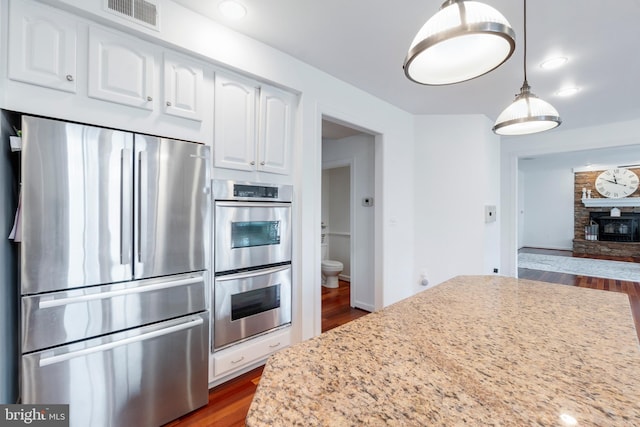 kitchen with light stone countertops, hanging light fixtures, stainless steel appliances, dark hardwood / wood-style floors, and white cabinets