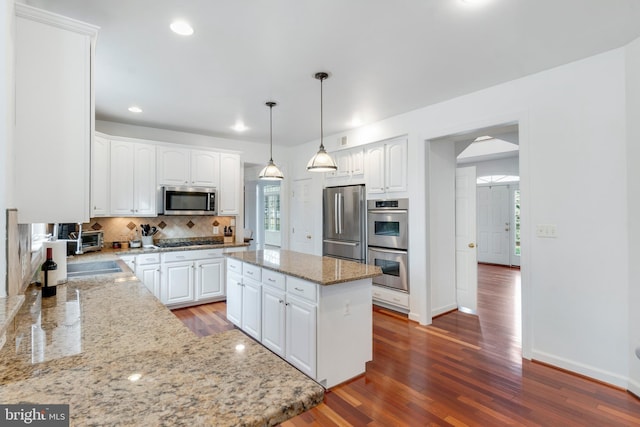 kitchen featuring light stone countertops, stainless steel appliances, decorative light fixtures, white cabinets, and a kitchen island