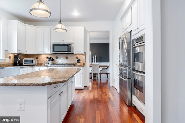 kitchen featuring white cabinetry, stainless steel appliances, tasteful backsplash, decorative light fixtures, and a kitchen island