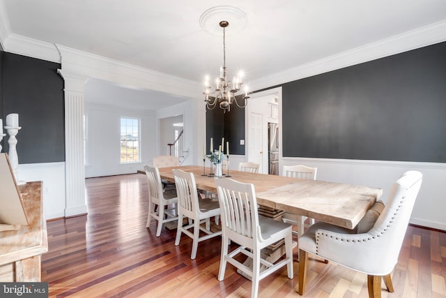 dining space featuring hardwood / wood-style floors, an inviting chandelier, crown molding, and ornate columns